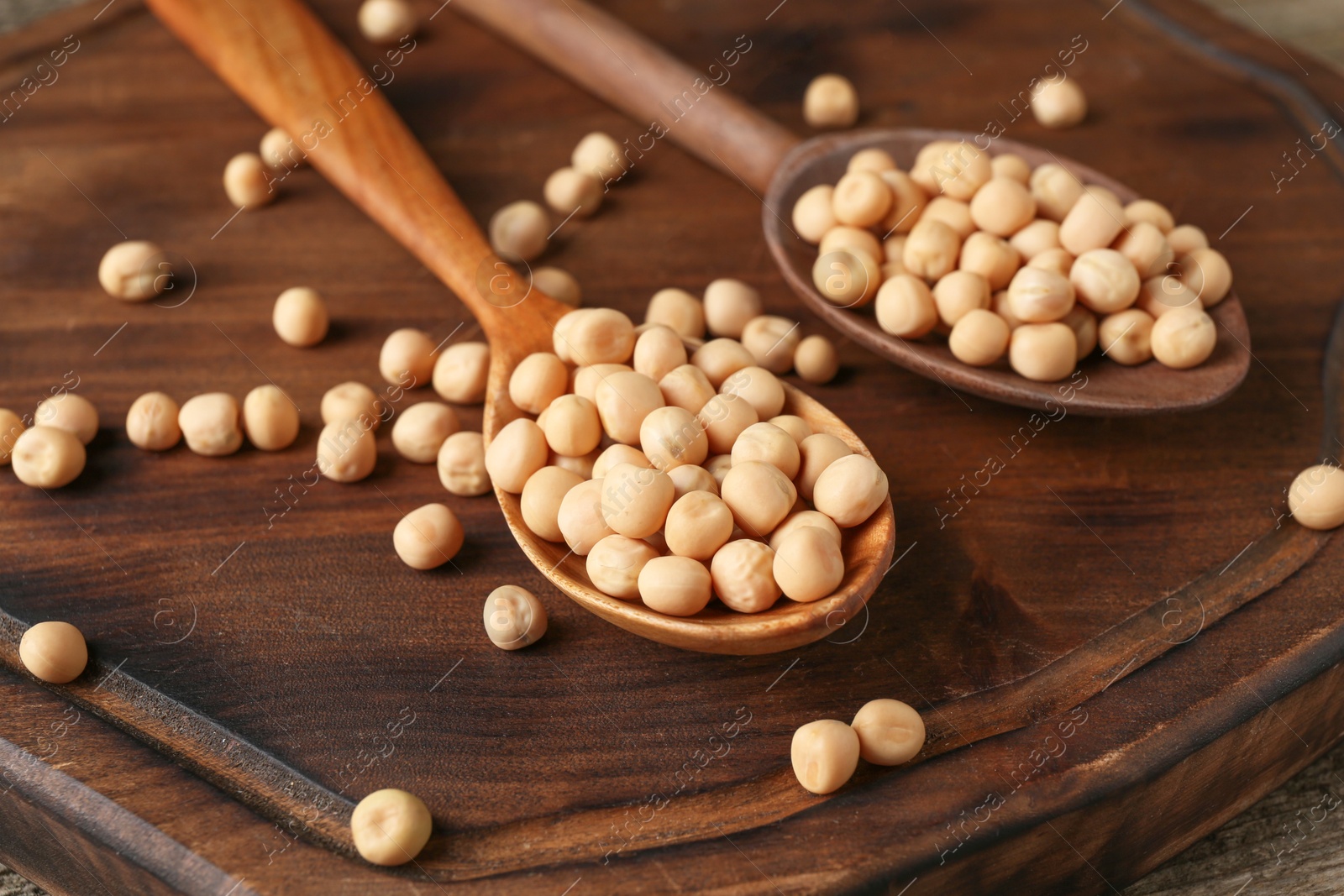 Photo of Spoons with dried peas on wooden table, closeup