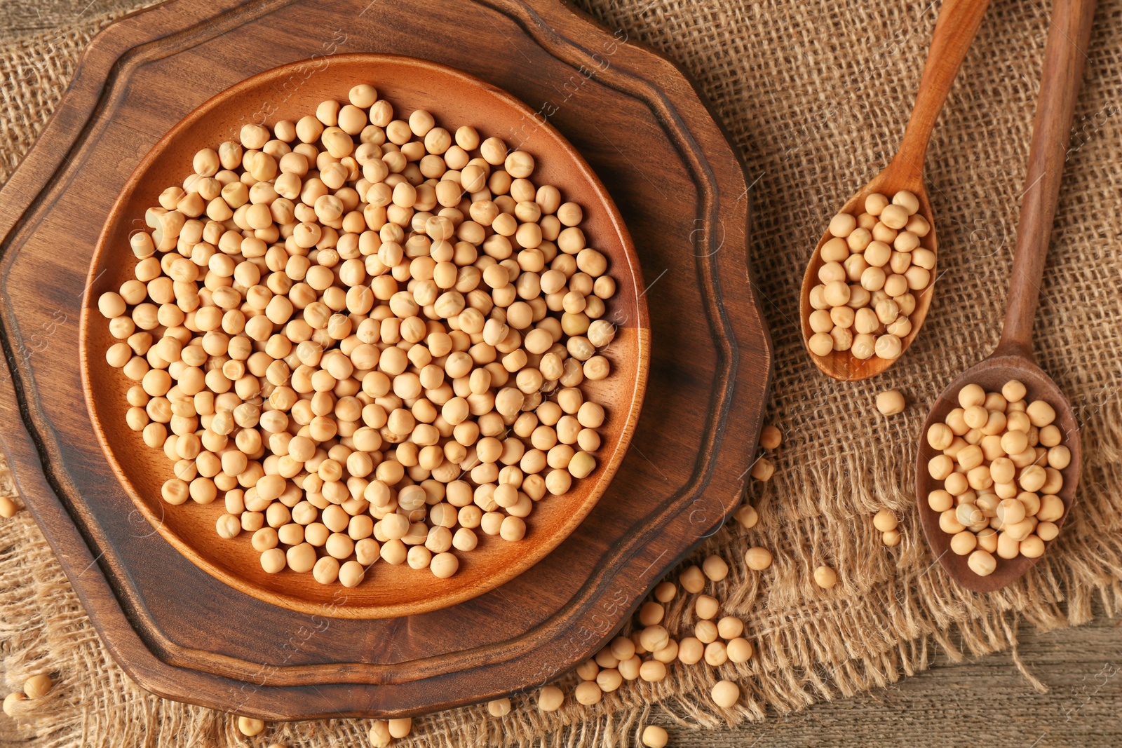 Photo of Dried peas, plate and spoons on wooden table, top view