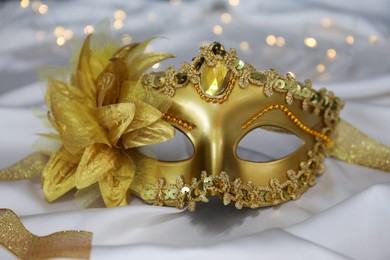 Photo of Beautiful golden carnival on white silk fabric, closeup