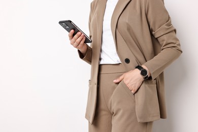 Woman in beige suit using smartphone on white background, closeup. Space for text