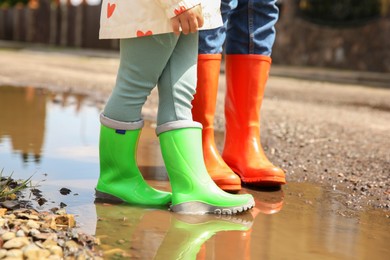 Photo of Mother and daughter wearing rubber boots standing in puddle outdoors, closeup