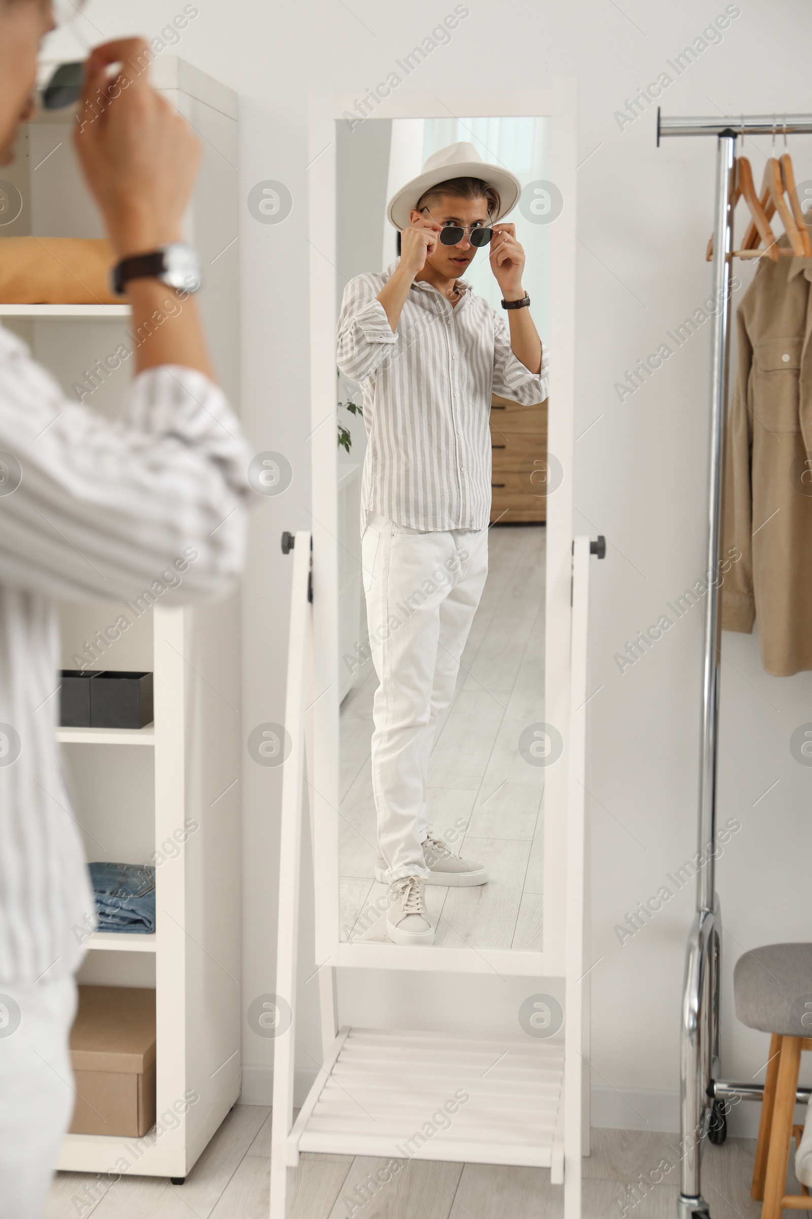 Photo of Handsome man in hat and glasses looking at mirror indoors