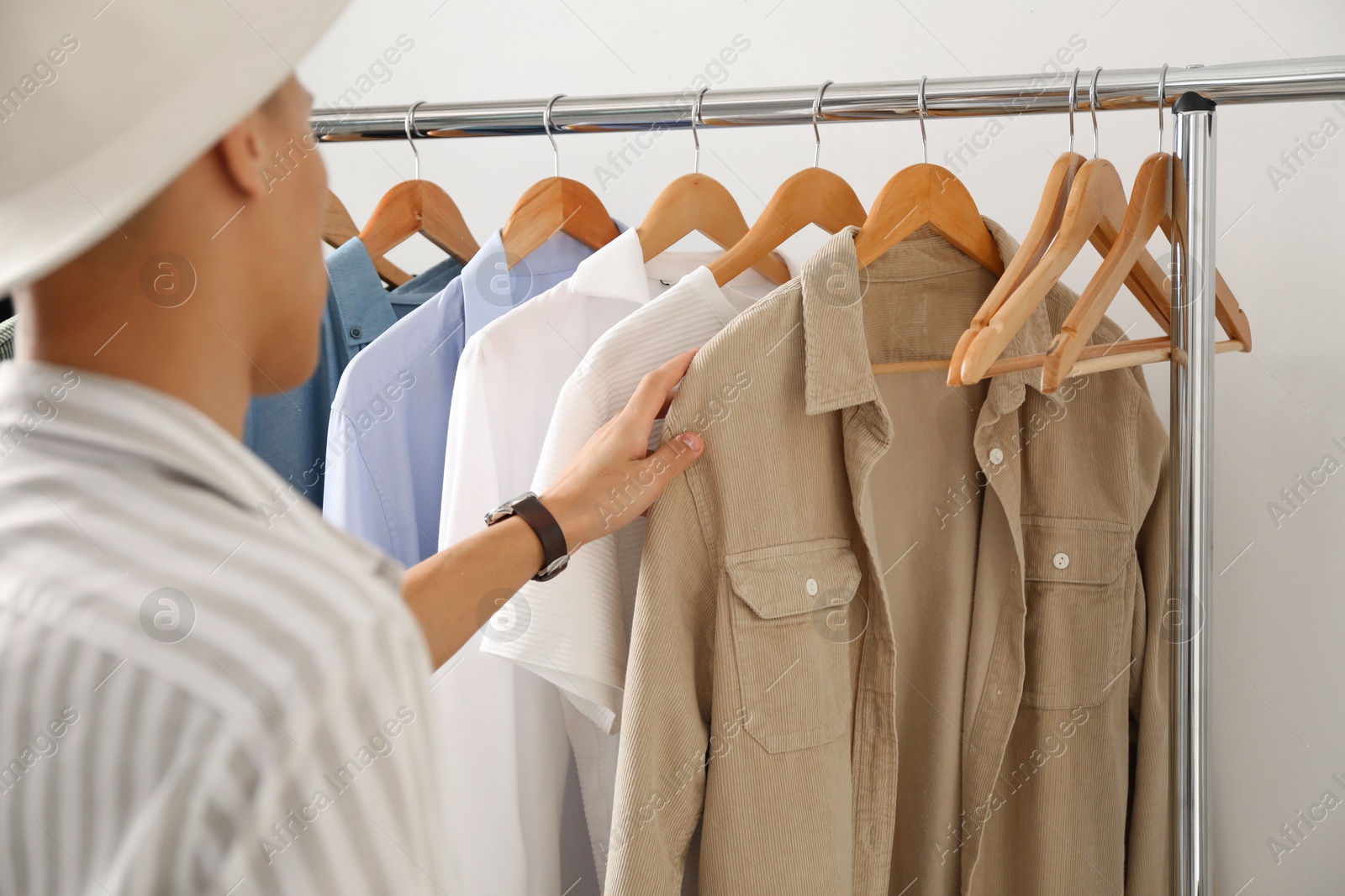 Photo of Man in hat choosing clothes near rack indoors