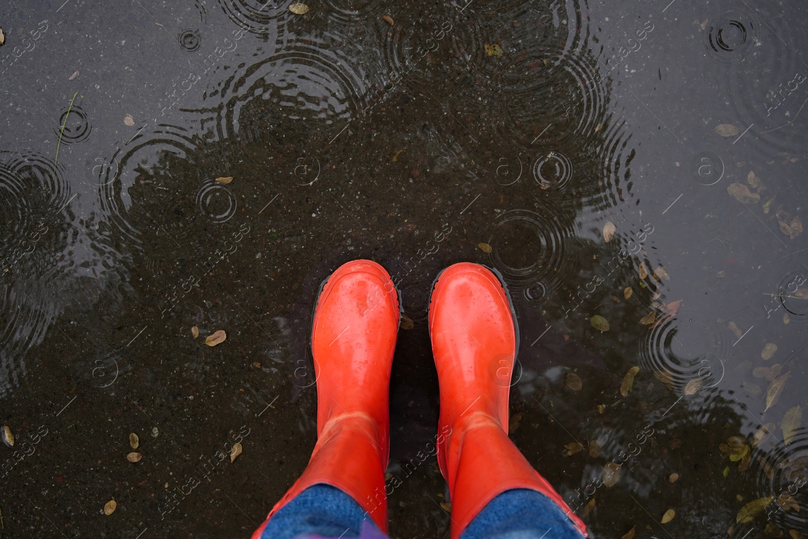 Photo of Woman wearing red rubber boots standing in rippled puddle, top view