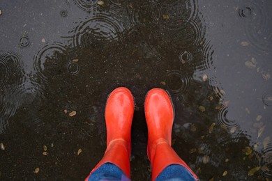 Photo of Woman wearing red rubber boots standing in rippled puddle, top view