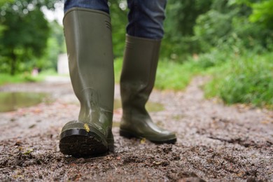 Photo of Woman in green rubber boots walking on muddy road, closeup