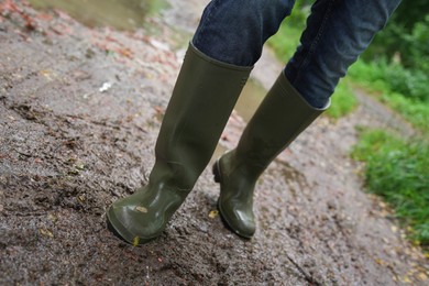 Photo of Woman in green rubber boots walking on muddy road, closeup