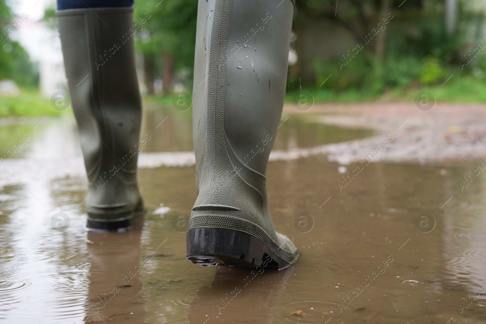 Photo of Woman wearing green rubber boots walking in puddle outdoors, closeup. Space for text