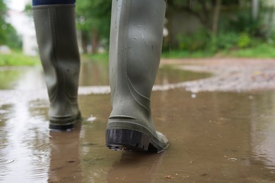 Photo of Woman wearing green rubber boots walking in puddle outdoors, closeup. Space for text