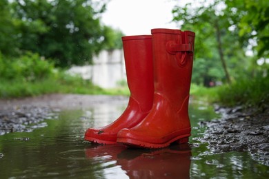 Photo of Red rubber boots in puddle at rainy day, closeup