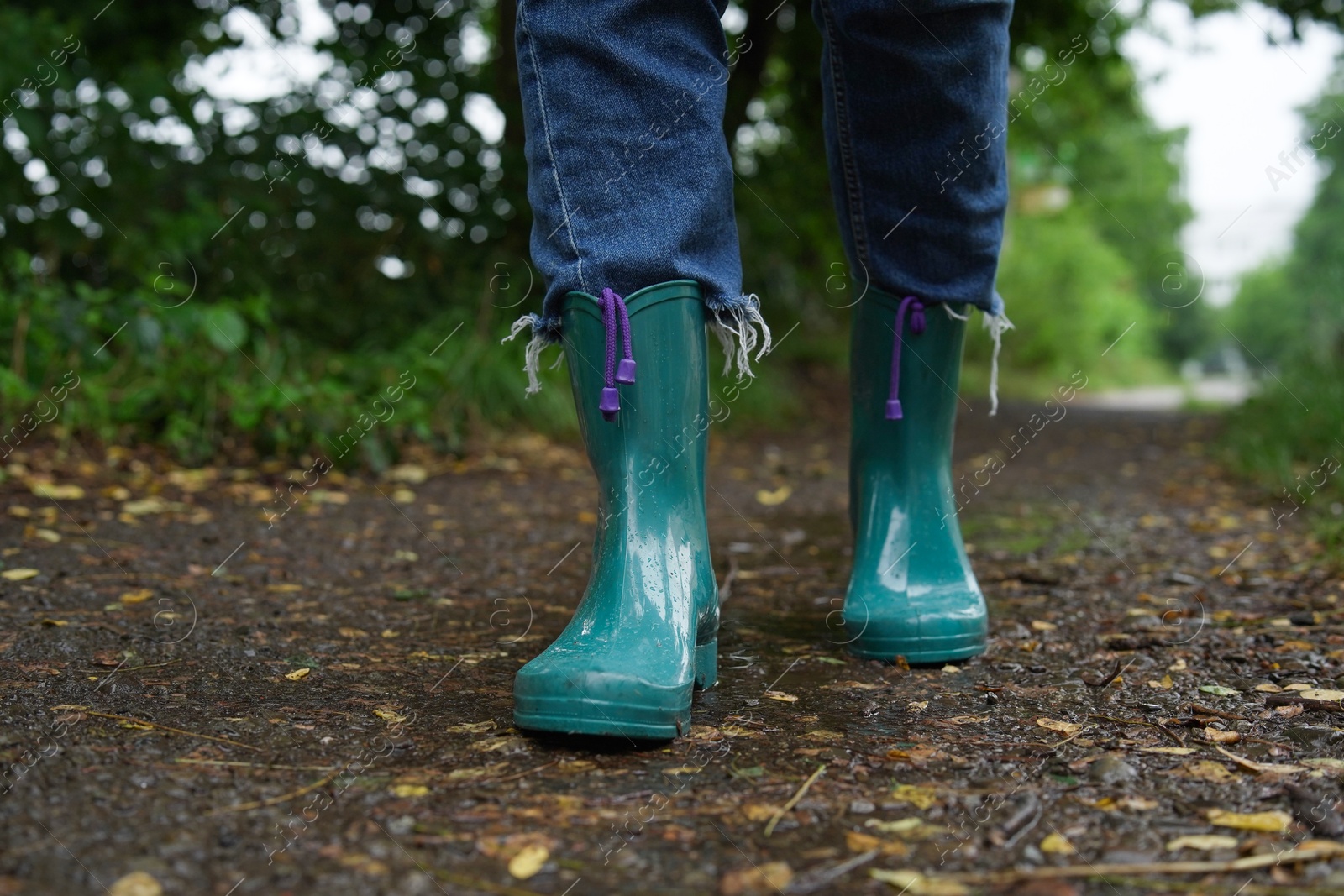 Photo of Woman in turquoise rubber boots walking on wet road, closeup