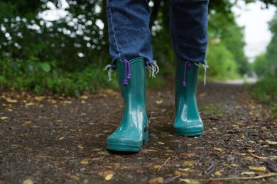 Photo of Woman in turquoise rubber boots walking on wet road, closeup