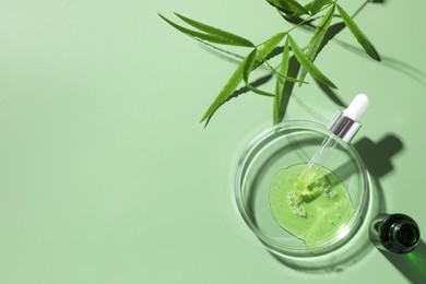 Photo of Petri dish with cosmetic product, bottle, pipette and leaves on green background, flat lay. Space for text