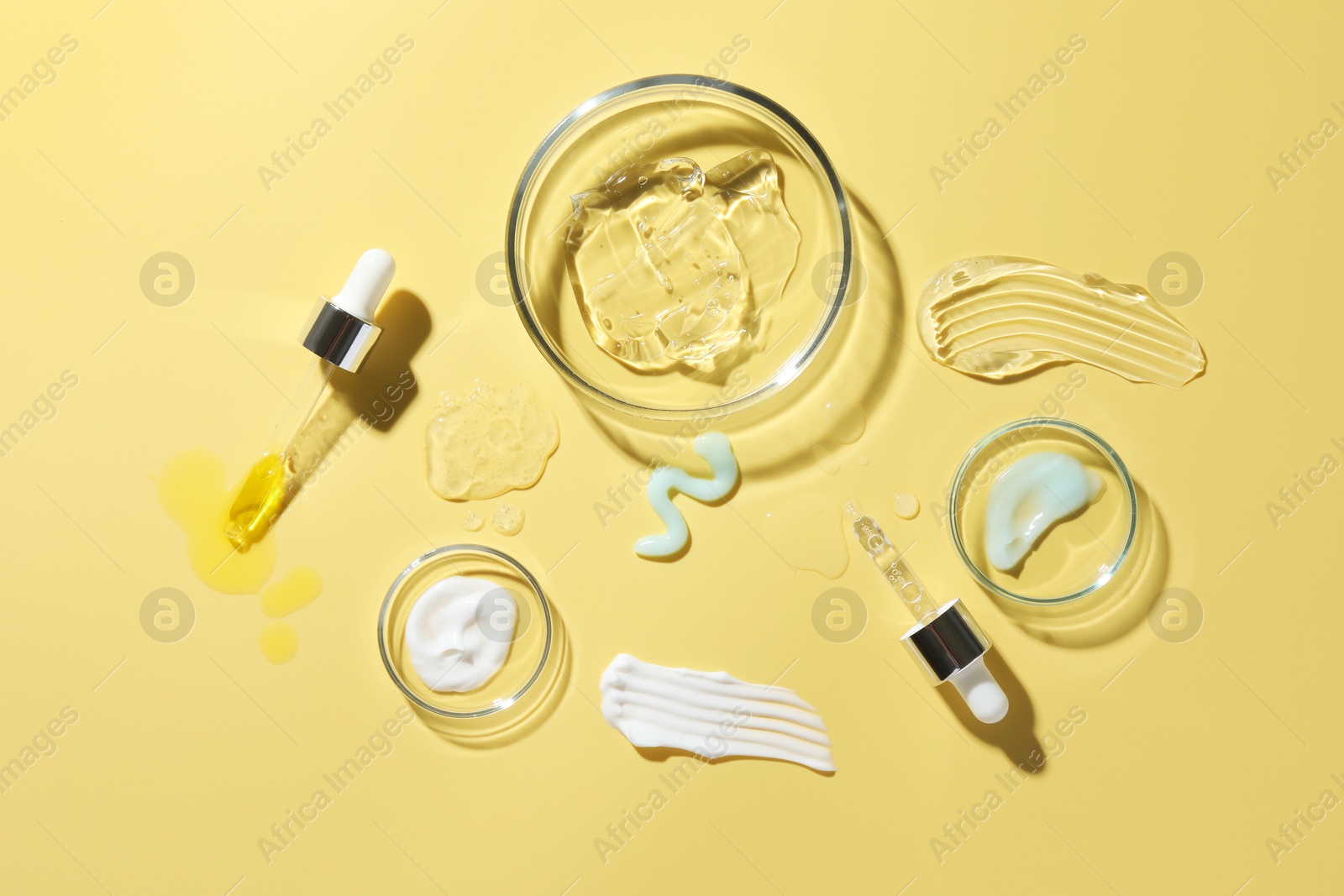 Photo of Petri dishes with cosmetic products and pipettes on yellow background, flat lay