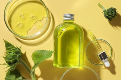 Photo of Petri dishes with cosmetic product, bottle, pipette and sunflowers on yellow background, flat lay