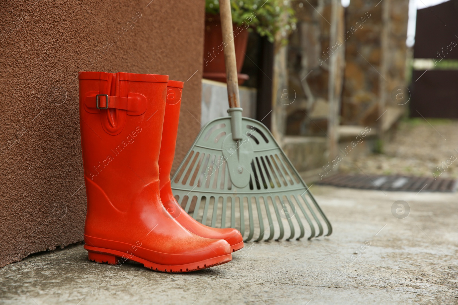 Photo of Orange rubber boots and rake near wall outdoors