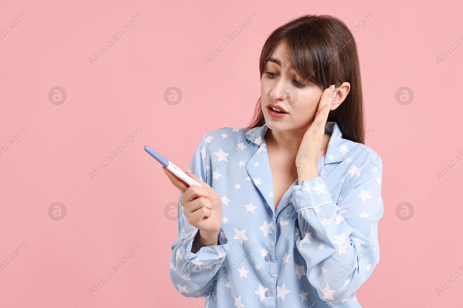 Photo of Worried young woman with pregnancy test on pink background, space for text