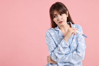 Worried young woman with pregnancy test on pink background, space for text