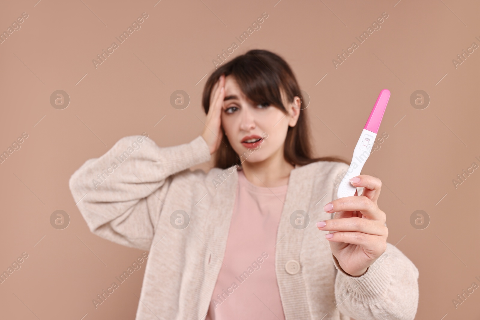 Photo of Worried young woman with pregnancy test on light brown background, selective focus