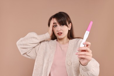 Worried young woman with pregnancy test on light brown background, selective focus