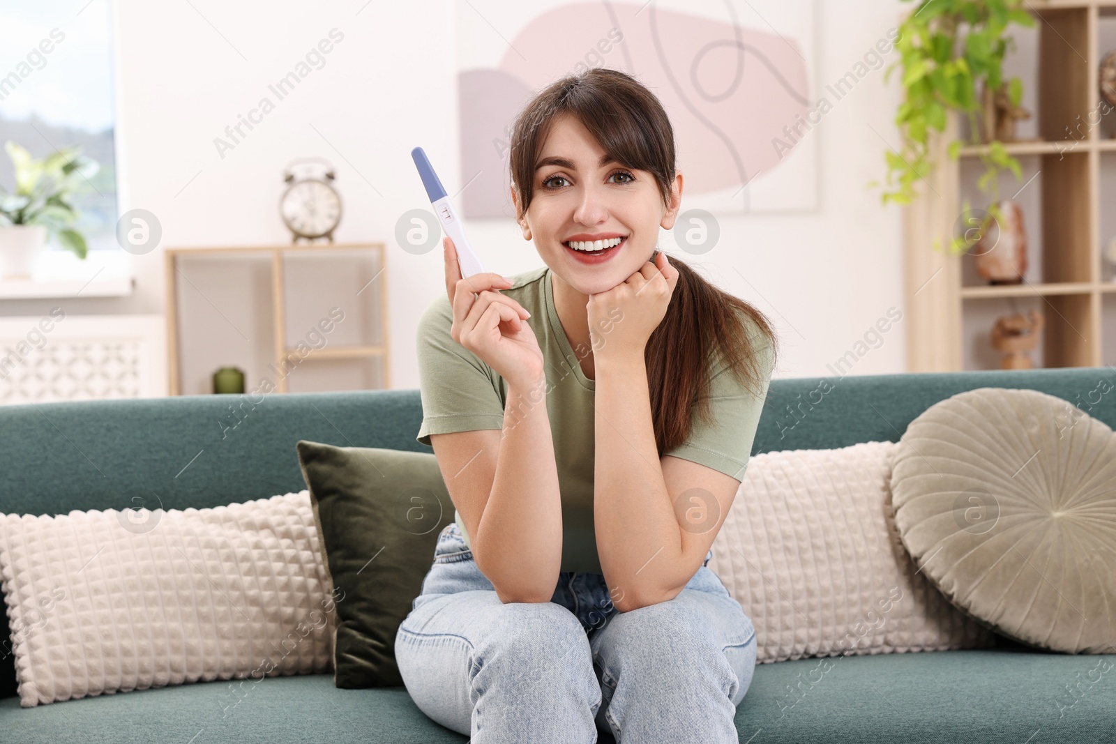 Photo of Happy young woman with pregnancy test on sofa at home