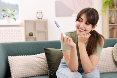 Photo of Happy young woman with pregnancy test on sofa at home, space for text