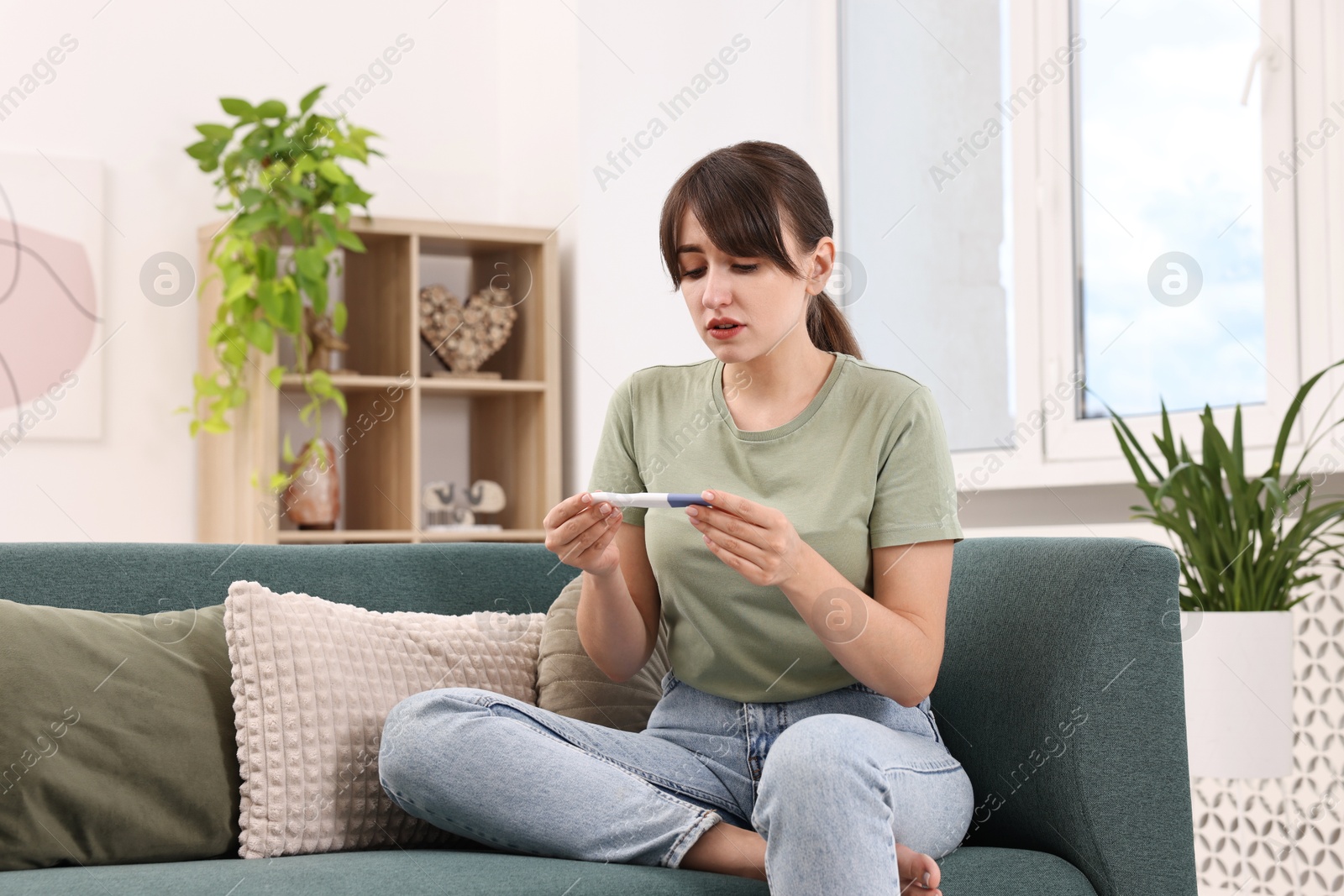 Photo of Worried young woman with pregnancy test on sofa at home