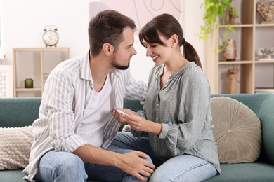 Photo of Happy young couple with pregnancy test on sofa at home