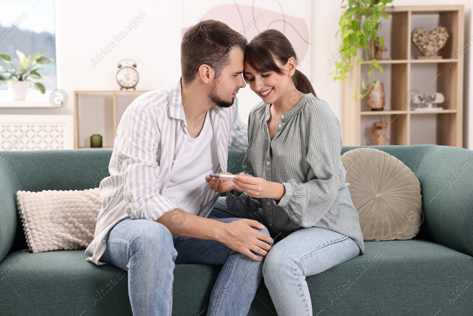 Photo of Happy young couple with pregnancy test on sofa at home