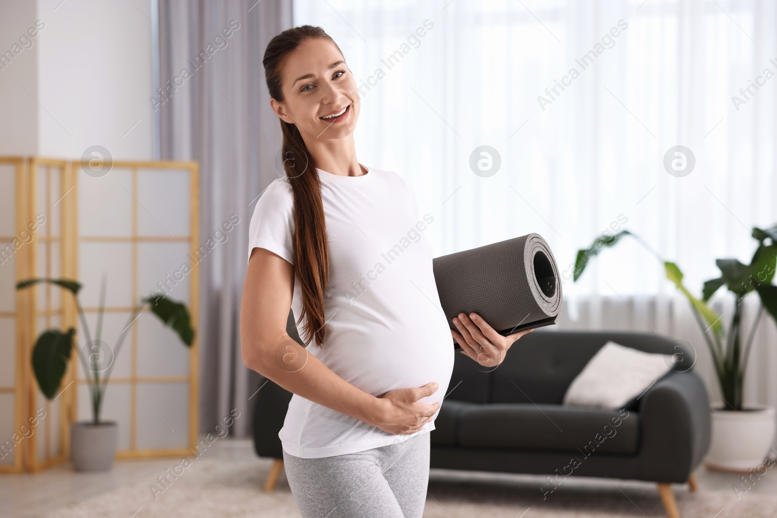 Photo of Smiling pregnant woman with exercise mat at home