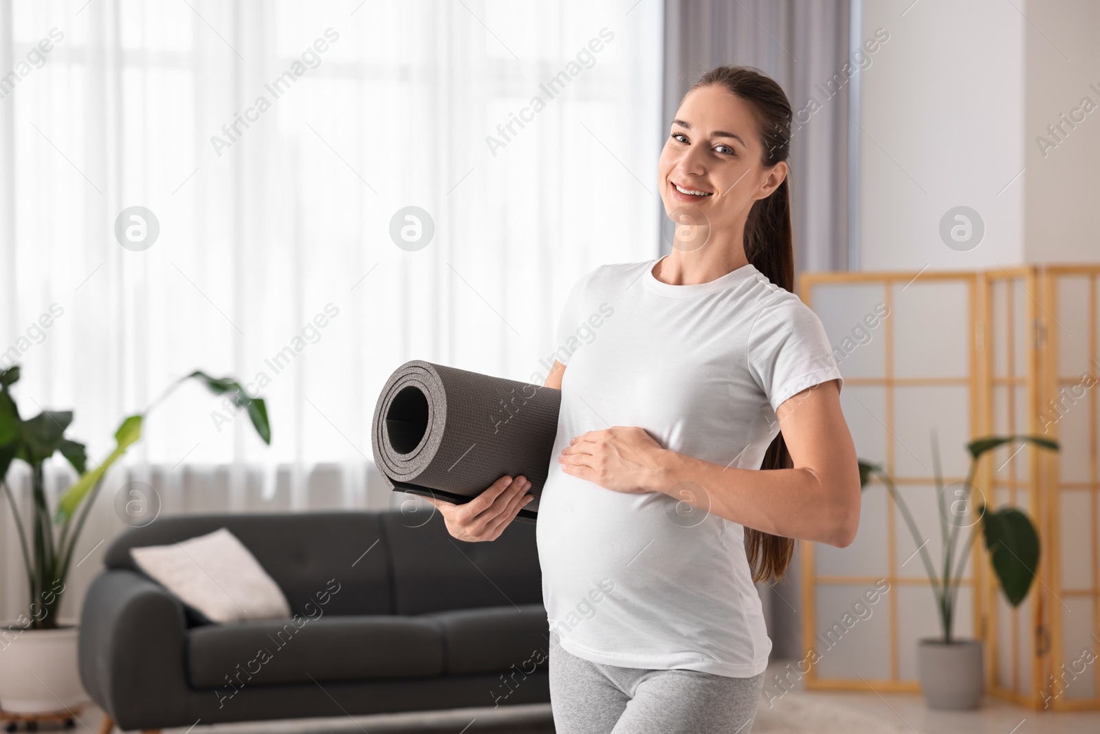 Photo of Smiling pregnant woman with exercise mat at home