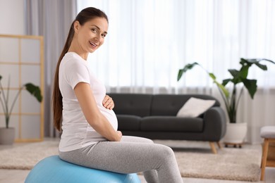 Beautiful pregnant woman doing exercises on fitball at home, space for text