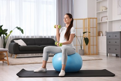 Beautiful pregnant woman with dumbbells doing exercises on fitball at home