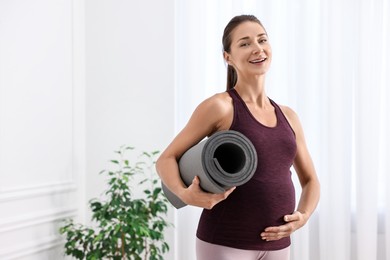 Beautiful pregnant woman with exercise mat at home