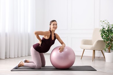 Beautiful pregnant woman doing exercises with fitball on mat at home