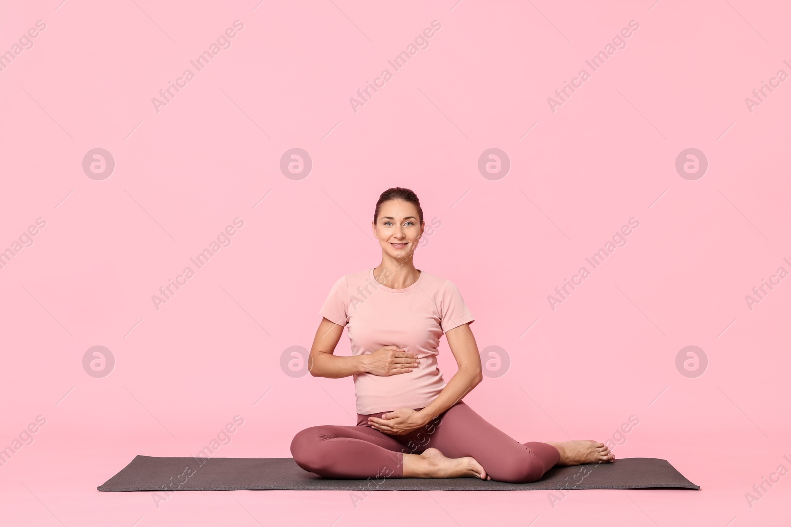 Photo of Beautiful pregnant woman on exercise mat against pink background