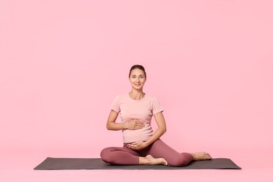 Photo of Beautiful pregnant woman on exercise mat against pink background