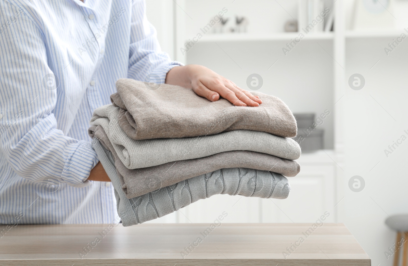 Photo of Woman with stack of clean clothes at wooden table indoors, closeup