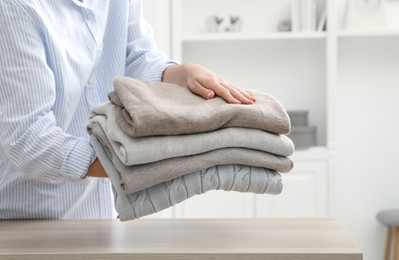 Photo of Woman with stack of clean clothes at wooden table indoors, closeup