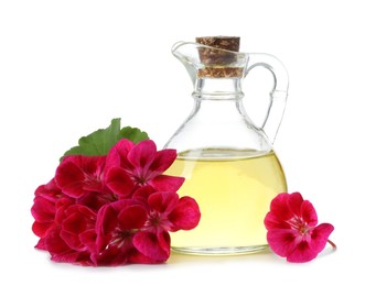 Photo of Geranium essential oil in jug and beautiful flowers isolated on white