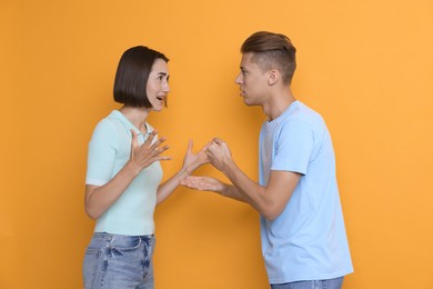 Emotional young couple arguing on orange background