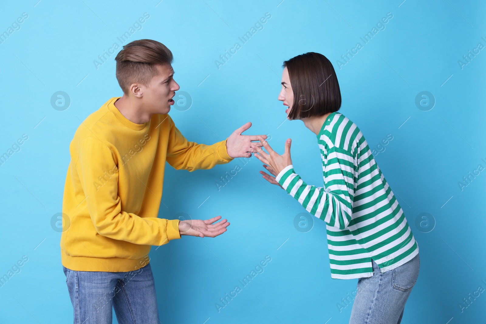 Photo of Emotional young couple having quarrel on light blue background