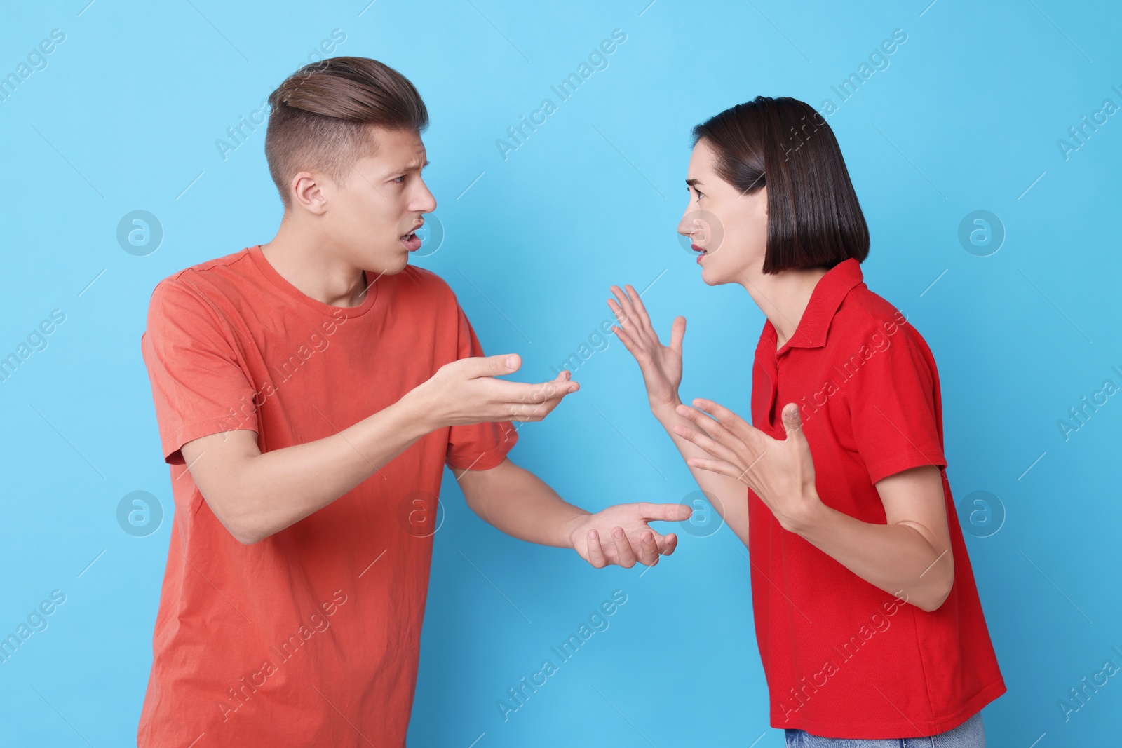 Photo of Emotional young couple having quarrel on light blue background