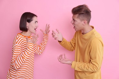 Emotional young couple arguing on pink background