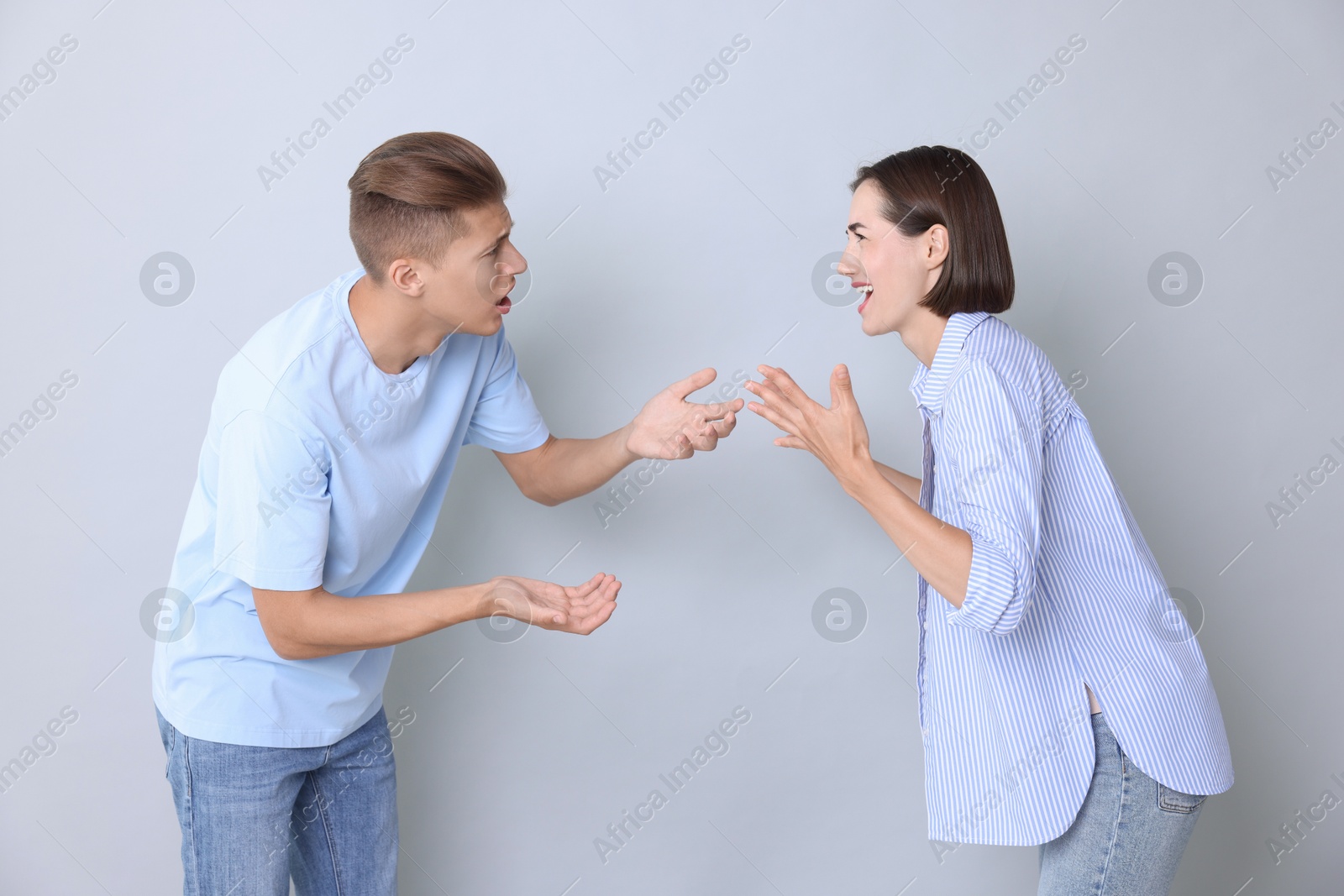 Photo of Emotional young couple having quarrel on grey background