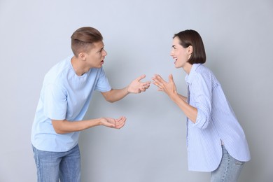 Emotional young couple having quarrel on grey background