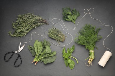 Photo of Different fresh herbs, spool of thread and scissors on grey textured table, flat lay