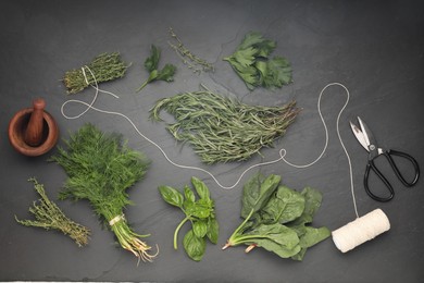 Photo of Different fresh herbs, spool of thread, mortar with pestle and scissors on grey textured table, flat lay