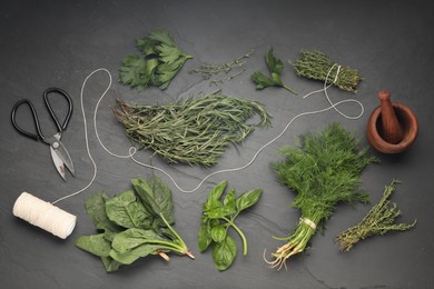 Different fresh herbs, spool of thread, mortar with pestle and scissors on grey textured table, flat lay