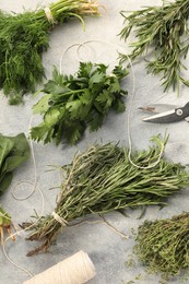 Photo of Bunches of different fresh herbs, thread and scissors on light grey textured table, flat lay